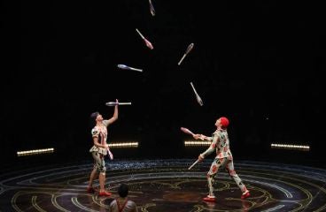 A stage scene featuring two individuals performing as jugglers within a circular ring, captivating the audience.